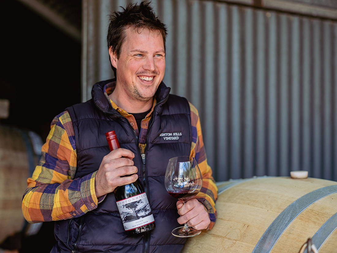 A smiling Liam van Pelt holding Ashton Hills Wine